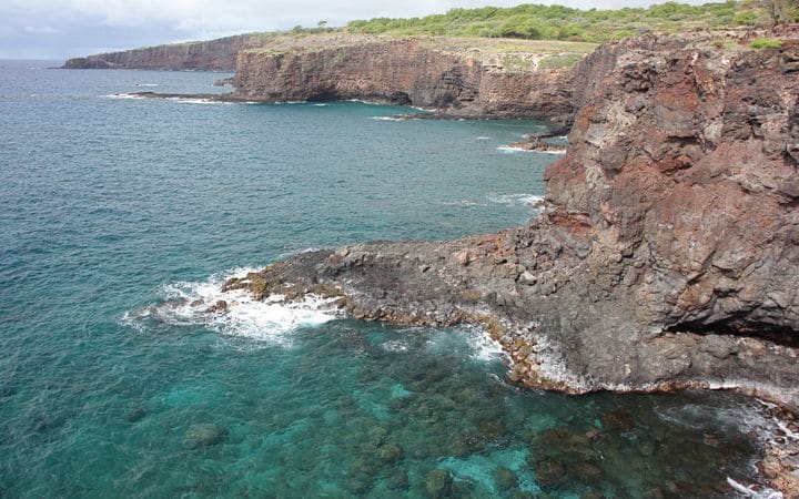 Red lava cliffs above clear turquoise water at Hulopoʻe Bay on Lānaʻi