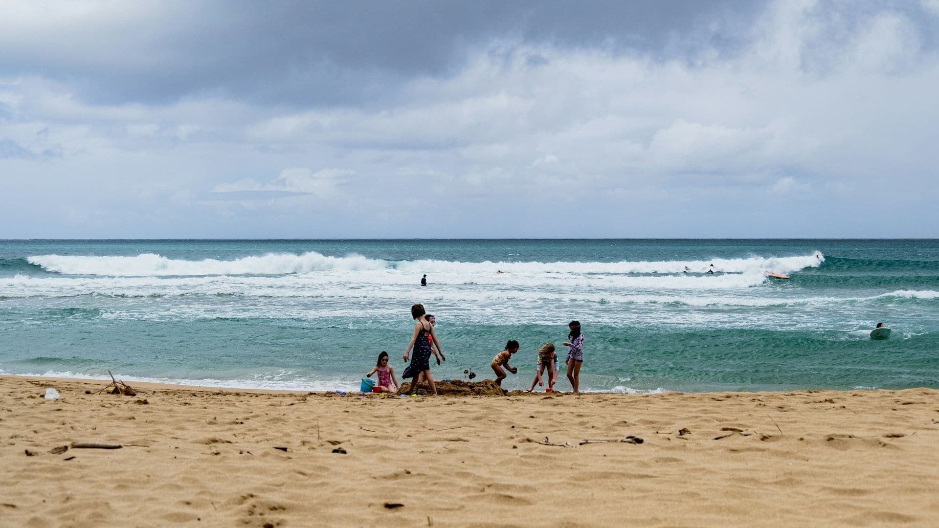 Families playing on the sand as waves roll in at Hanalei Beach